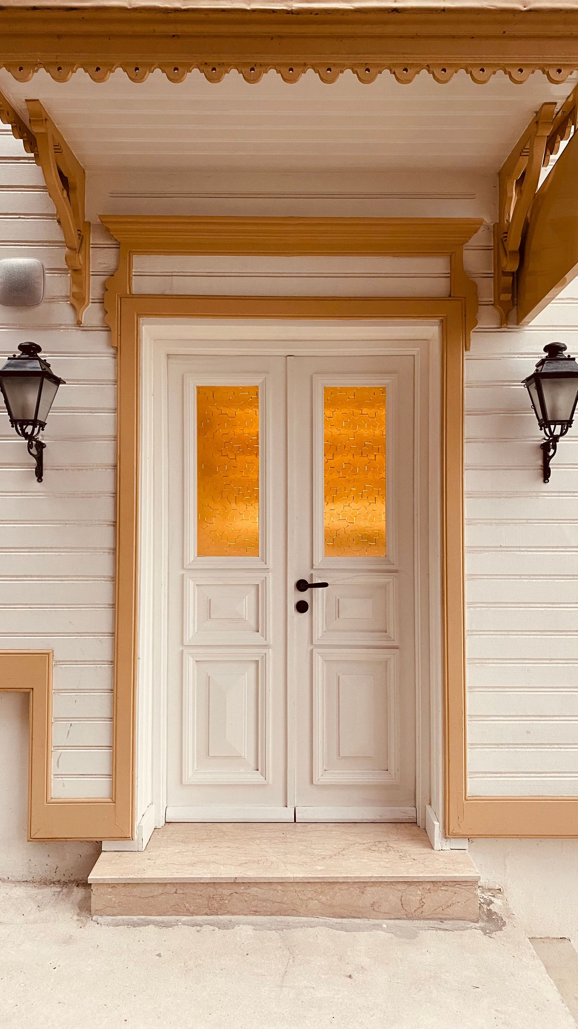 Front view of a classic wooden door with decorative yellow glass panes and wall lamps.